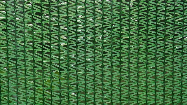 Close View of Green Shade Net for Plants with Rain Drops Sliding Down Woven Mesh, Detailed Texture Showing Sun Protection And Outdoor Gardening