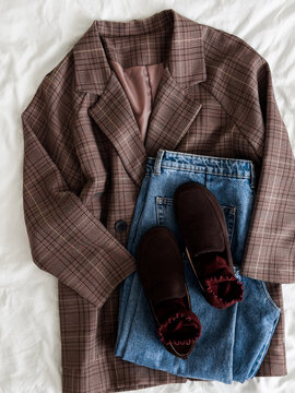 A checkered blazer, blue jeans, brown suede loafers on a light background, top view. Comfortable women's casual clothing