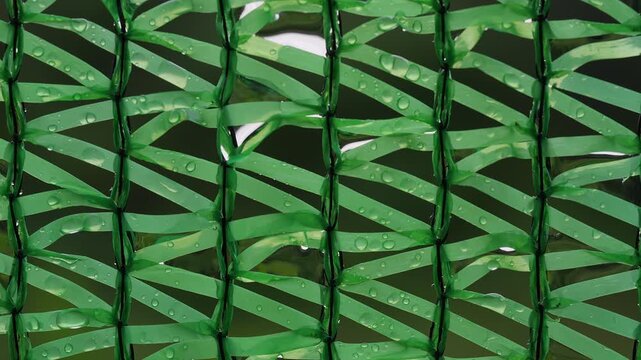 Green Woven Plastic Mesh Holds Clear Water Droplets in a Close Up Abstract Background, Showing Freshness and Texture