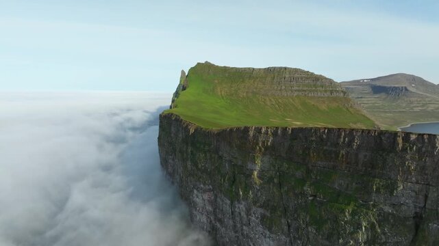 A captivating aerial drone push in shot reveals the dramatic "Horn" seacliff and lush green landscape of Hornstrandir Nature Reserve on Iceland. Coastal fog shrouds the rugged Westfjords.