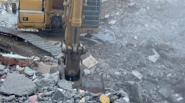 Excavator bucket crushes concrete rubble on demolition site. Heavy machine shifts debris and dust as bucket grips broken slabs, clearing damaged ground in gritty industrial work with forceful motion.