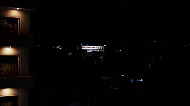 Warm-lit windows on a nearby building contrast with distant lights in Rishikesh at night.