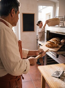 B&auml;cker schiebt frisch gebackenes Brot mit Holzschieber aus dem Ofen