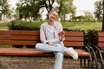 Fototapeta premium Happy man finding calm and joy in nature while using phone in green park