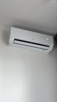 Air conditioning unit activated by a remote control to set temperature to 24 degrees. Hand uses wireless controller to change mode for seasonal cooling or heating purposes. Wall mounted white split