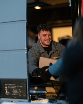 Parcel being handed over by a delivery worker during a freezing winter snap, featuring frosty air and a dark street for last-mile delivery