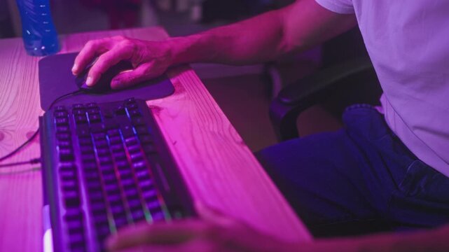 Man with right hand on mouse and left on keyboard at studio desk under purple lighting; concentration.