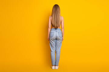 Obraz premium Portrait of a stylish young woman in casual outfit posing against a vibrant yellow background in relaxed stance