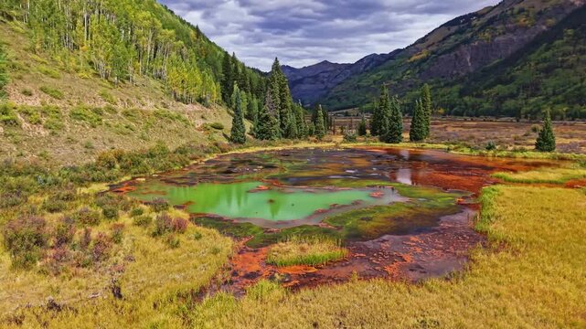 Golden autumn aspen forests and rugged mountains surround colorful mineral ponds near historic Ironton along Million Dollar Highway Colorado