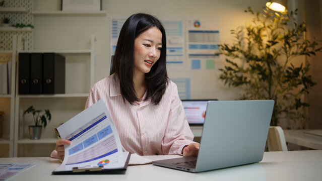 Asian businesswoman comparing printed financial reports at her desk.