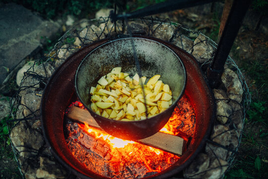 Chopped potatoes cooking in a cast iron cauldron over open campfire flames