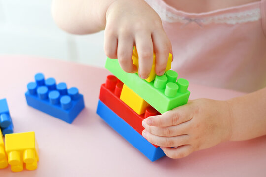 Child&rsquo;s hands building with colorful plastic blocks on a pink table. Ideal for educational materials, neurodevelopmental resources, preschool ads, parenting guides, and toy catalogs.
