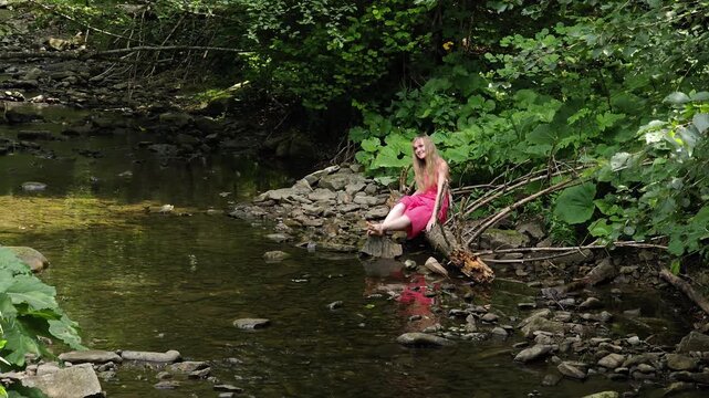 Smiling woman sitting on riverbank and throwing stone into water