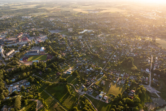 Small town, stadium and houses in golden sunset haze from above. High altitude drone shot of small town at summer sunset in golden haze: football stadium with running track, apartment blocks.