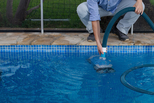 Pool worker operating water cleaning equipment at swimming pool with copy space