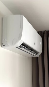 Horizontal air louver moving back and forth on a working split system air conditioner. White automated vent flap opens and closes dynamically to regulate room ventilation during handheld shooting.