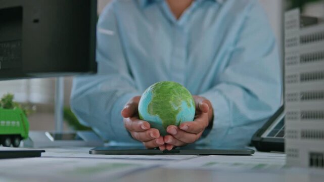 Businesswoman holding a green globe, ESG concept (Environmental, Social, and Governance), reviewing ESG reports and green financial charts, sustainability, love the earth, and eco-friendly.