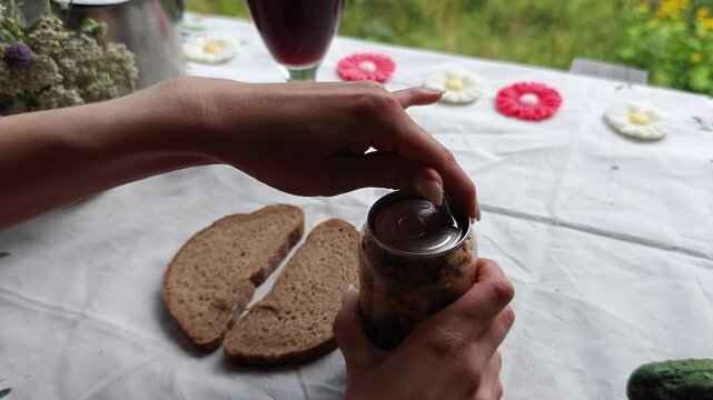Hands open a metal pull ring lid on a glass jar of pork fat.