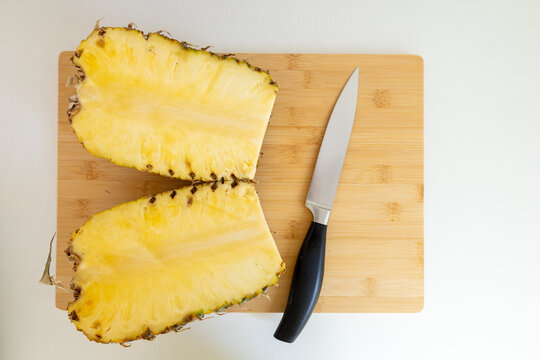 fresh pineapple cut in half on cutting board with knife