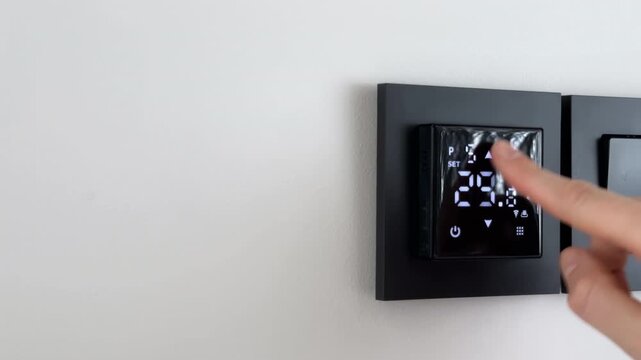 Underfloor heating thermostat switched off by human finger on a black smart digital interface. User interacts with modern wall mounted touch controller panel to deactivate climate temperature system.