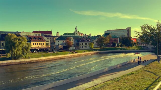 River embankment in Minsk on sunset, views of pedestrian Bridge. Pleasure boat speeds through water while buildings background. Svisloch River flows through historic center of city. 