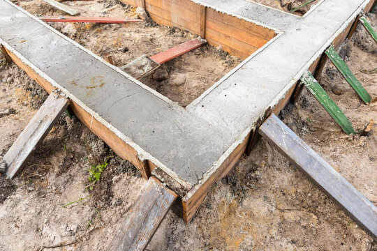 Concrete foundation footings poured into wooden formwork at a residential construction site, showing bracing, soil, and early-stage building layout for a new house foundation and structural base