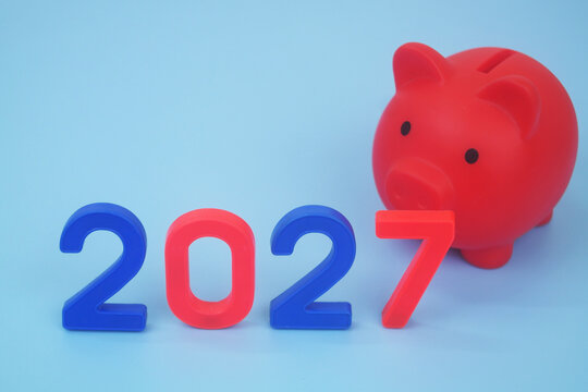 Piggy bank and numbers 2027 on blue background. Saving and investments n year 2027 concept.