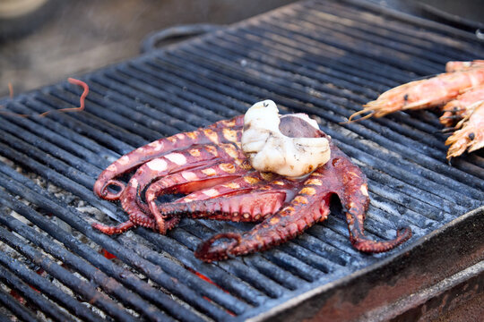 Fresh octopus and prawns cooking on a hot charcoal grill at a traditional Sicilian fish market of La Pescheria in Catania.