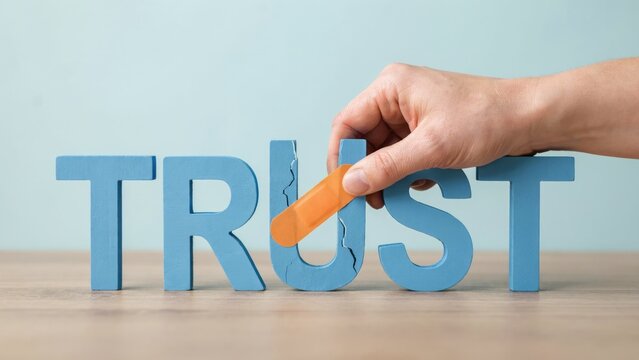 Hand applying an adhesive bandage to a cracked blue wooden letter u in the word trust