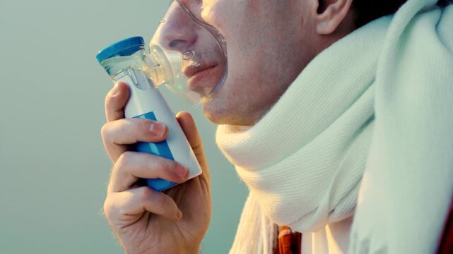 Sick man using nebulizer inhaler for home respiratory inhalation treatment of cough, cold, flu, and viral illness. High quality 4k footage