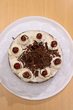 Vista superior de pastel tipo selva negra con virutas de chocolate central, crema y cerezas sobre plato blanco.