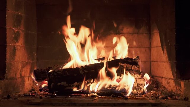 Burning wooden logs with flames and hot glowing embers inside a home fireplace. Cozy winter atmosphere and warm fire indoors.