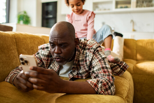 Man using smartphone while child sits on his back at home