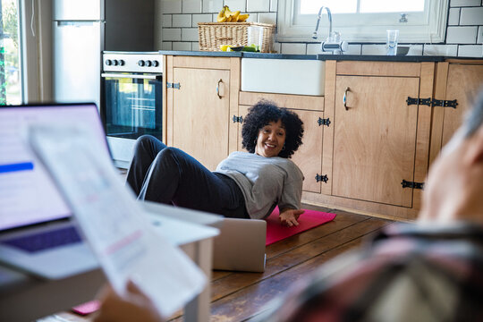 Smiling woman doing sit-ups on a yoga mat in the kitchen