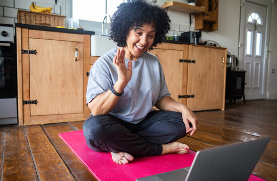 Woman waving to laptop on yoga mat in kitchen