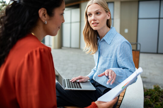 Two women reviewing a report outdoors with laptop