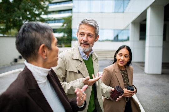 Business colleagues walking and talking with coffee outside office