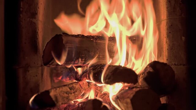 Burning wooden logs with flames and hot glowing embers inside a home fireplace. Cozy winter atmosphere and warm fire indoors.