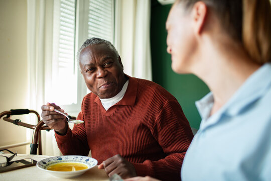 Senior man eating soup with caregiver