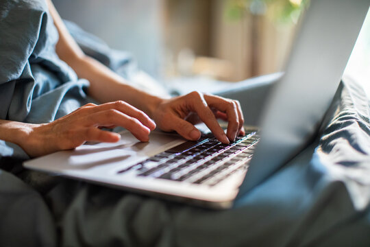 Hands typing on laptop in bed at home