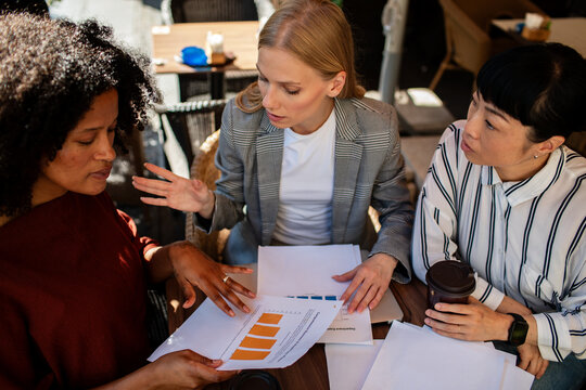 Three businesswomen reviewing charts at an outdoor cafe