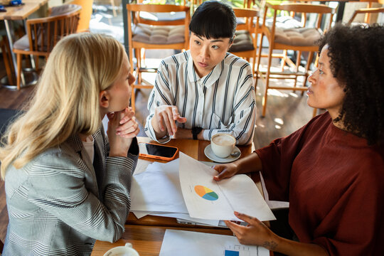 Three colleagues discuss a pie chart at a cafe