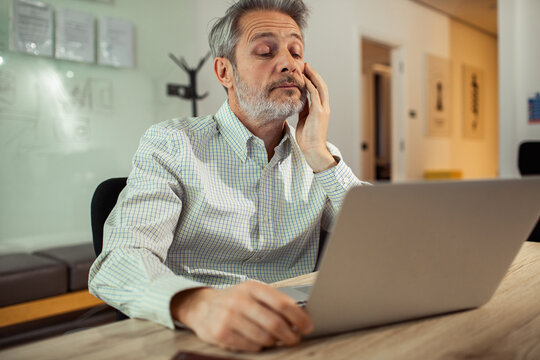 Tired mature man rubbing face while working on laptop