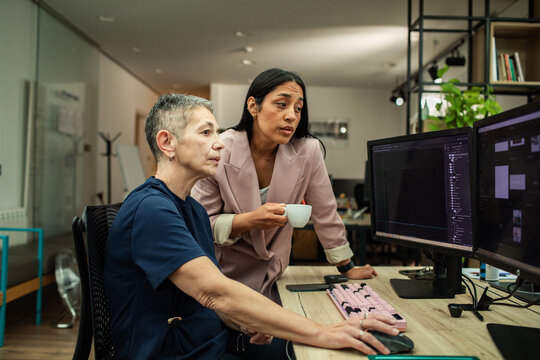 Coworkers reviewing edits on dual monitors in office