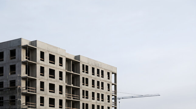 Un immeuble chantier en construction avec du b&eacute;ton brut et des grues sur fond de ciel clair et lumineux.