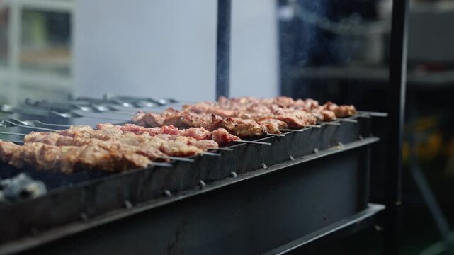 Meat skewers grilling on barbecue grill with rising smoke. Juicy kebab cooking on skewers over charcoal. Street food and outdoor cooking concept