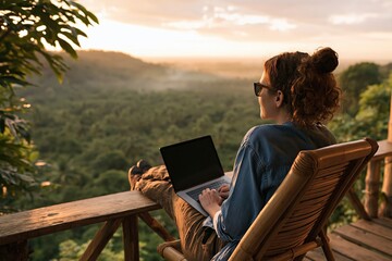 Obraz premium Woman using laptop on wooden balcony overlooking tropical forest at sunrise