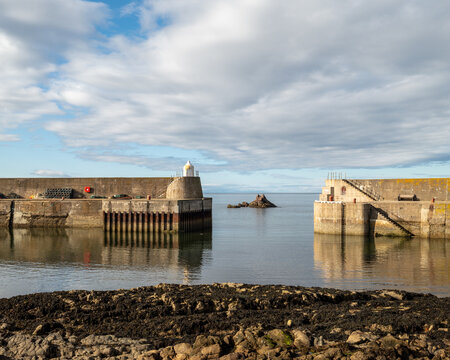 Calm waters surrounding the stone walls at the exit from Findochty Harbour in Scotland during a bright and cloudy afternoon under a wide sky