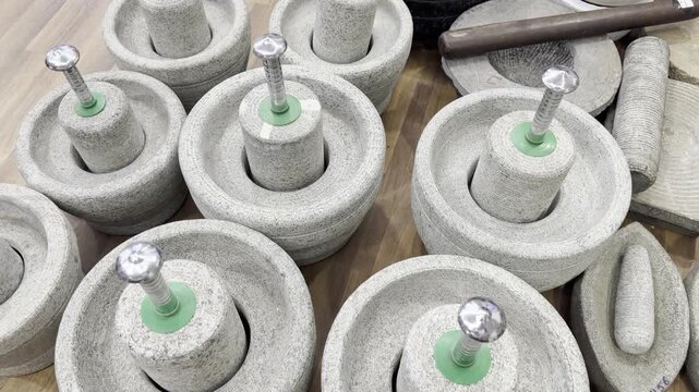Traditional stone mortar and pestle sets displayed in a kitchenware store, showing heavy granite grinding tools for crushing spices, herbs and ingredients used in cooking and food preparation. in use.