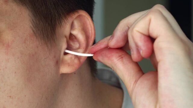 A man is cleaning earwax from his ears with a cotton swab.
Removing earwax plugs, hygiene, and morning routines.